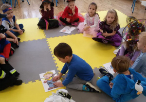 Widok na siedzące na dywanie dzieci. Oluś układa z części obrazek przedstawiający smerfa.
